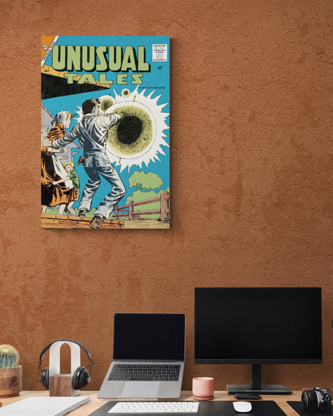 A large matte paper poster of the cover of the 1958 comic book "Unusual Tales #12" above a computer workstation containing a macbook, large monitor, headphones, camera, and a succulent