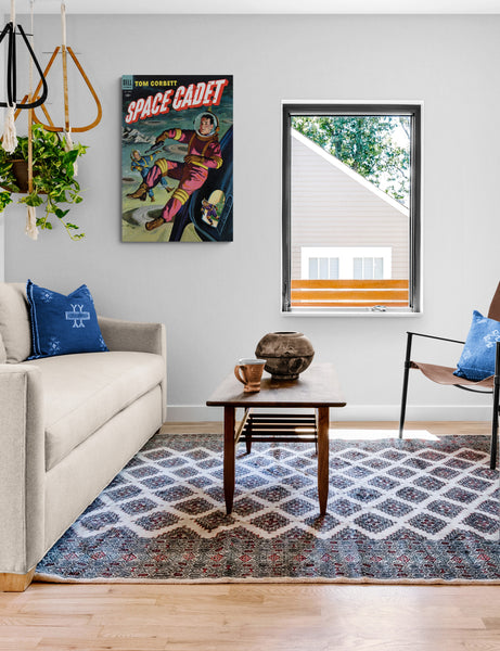 A large matte paper poster of the cover of the 1954 comic book "Space Cadet #9" hung in a minimalist living room containing a rug, sofa, and some plants