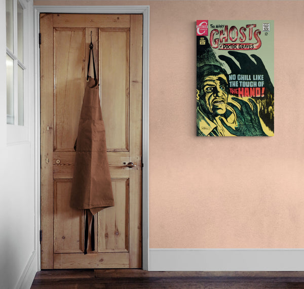 A large matte paper poster of the cover of the 1968 comic book "The Many Ghosts of Doctor Graves" hung on an old beige wall next to a rustic wooden door with an apron on it